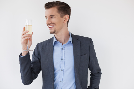 Closeup of joyful young handsome business man looking away and toasting with glass of wine. Isolated view on white background.