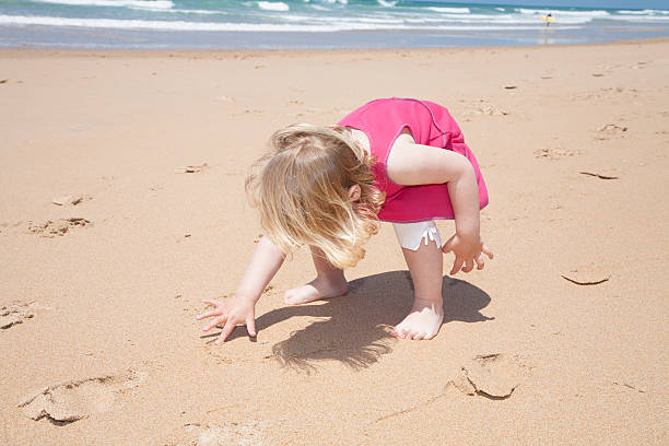 istock little girl crouch and writing with finger on sand beach 636799212