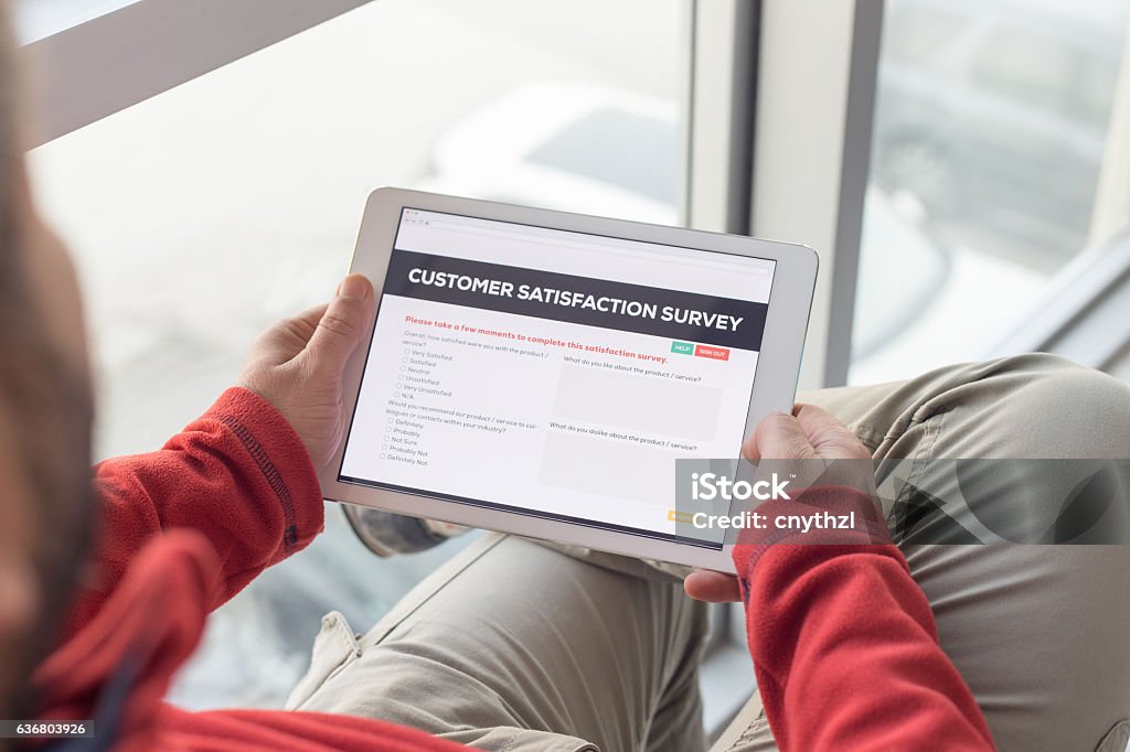 Man working on tablet with Customer Satisfaction Survey on screen Adult Stock Photo