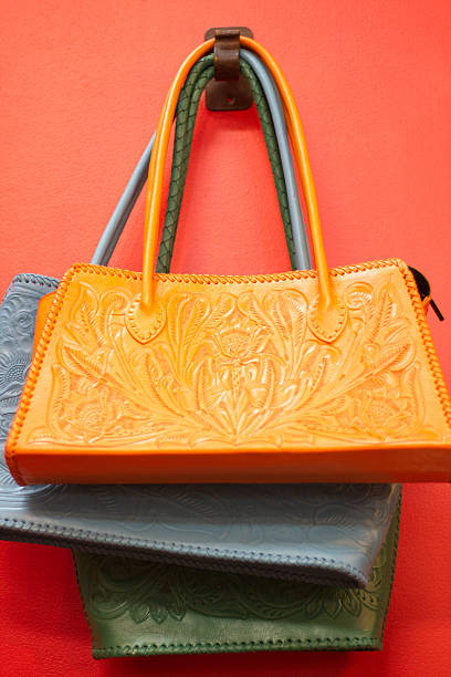 Traditional Mexican leather purses (orange, green, and gray) hang against a vibrant orangish-red wall.  Some copy space available at the top of the frame.