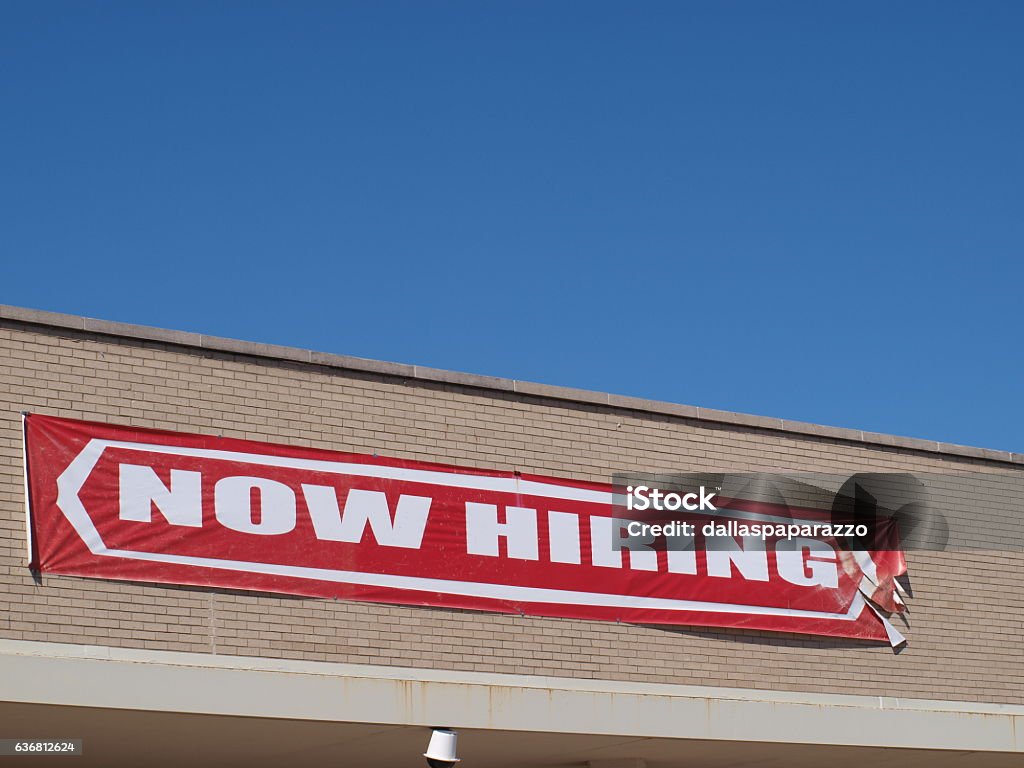 Now Hiring Sign A now hiring sign hangs on the side of a building in Dallas. Job signs are in demand for construction workers especially.  Help Wanted Sign Stock Photo