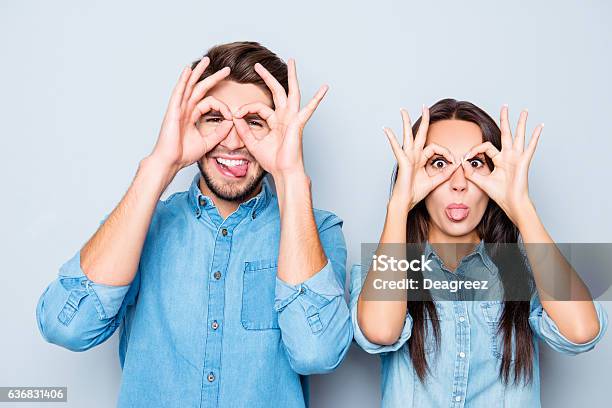 Pareja Feliz Haciendo Gafas Con Los Dedos Y Mostrando La Lengua Foto de stock y más banco de imágenes de Fondos