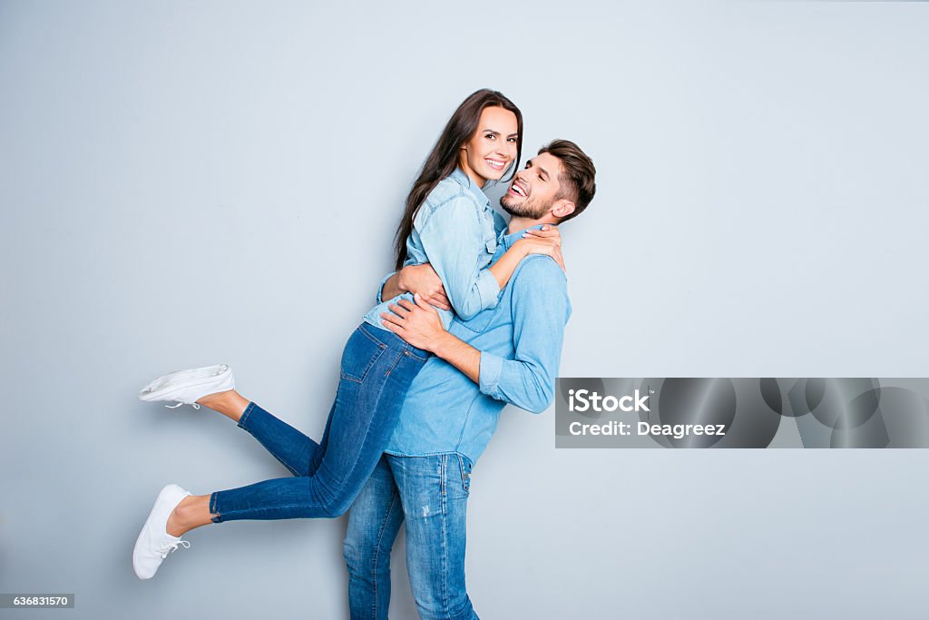 Hombre feliz llevando a su bonita esposa sobre fondo gris - Foto de stock de Parejas libre de derechos