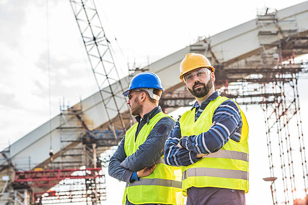istock Two successful brdge builders near construction platform with arms crossed 636832926