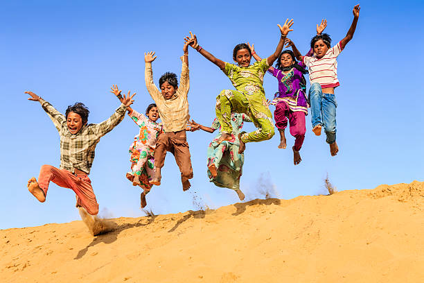группа happy индийских детей прыгает вниз дюна в песок - hinduism teenager female indian ethnicity стоковые фото и изображения