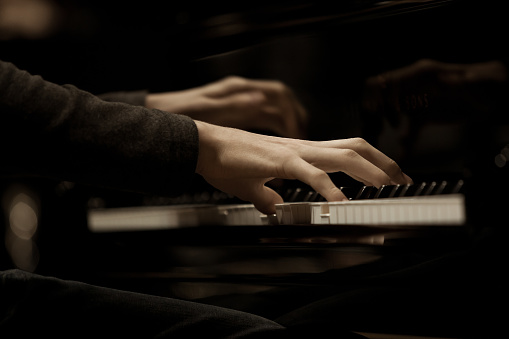Hands musician playing the piano closeup in dark colors