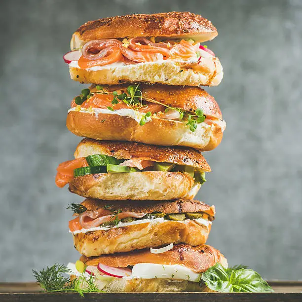 Heap of Bagels with salmon, eggs, vegetables, capers, fresh herbs and cream-cheese, grey concrete background, square crop. Healthy breakfast, lunch or take-away food concept