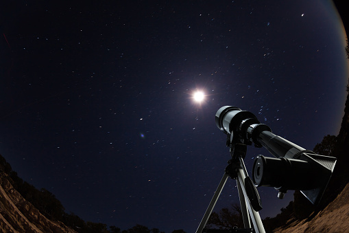 Telescope standing in the desert high mountains in the night pointing to the clear sky with stars and moon