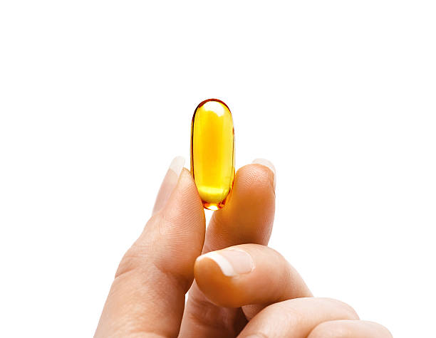 frauenfinger zeigen eine kapsel omega 3 - cod liver oil fish oil vitamin e vitamin pill stock-fotos und bilder