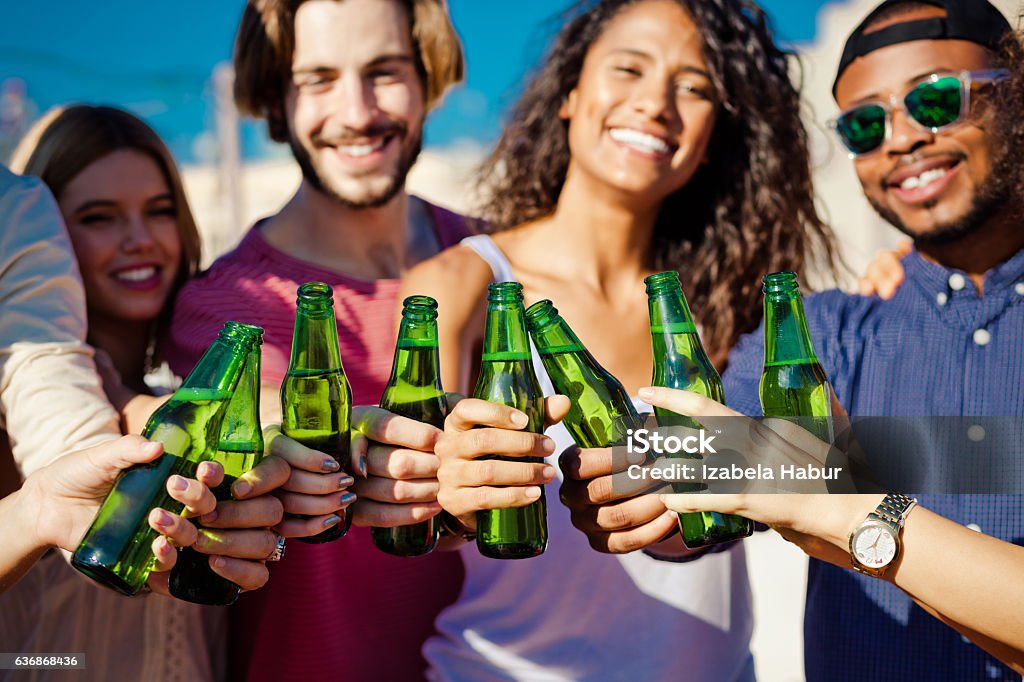 Happy friends drinking beer outdoors Outdoor party, group of happy friends toasting with beer bottles. Focus on hands. Adult Stock Photo