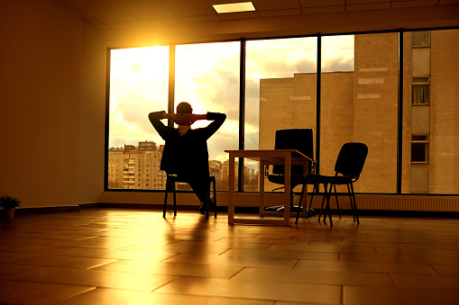 The concept of a business dream relaxation solutions. Businessman on  chair looking out window in modern office at sunset  sunlight.
