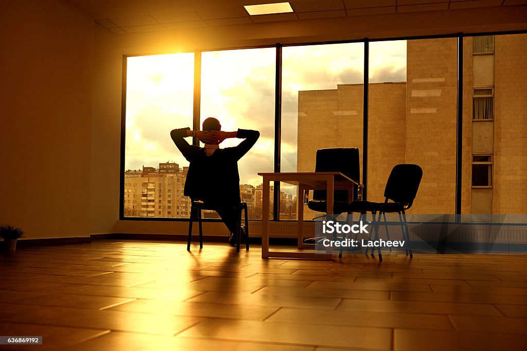 The concept of a business dream relaxation solutions. Businessma The concept of a business dream relaxation solutions. Businessman on  chair looking out window in modern office at sunset  sunlight. Zen-like Stock Photo