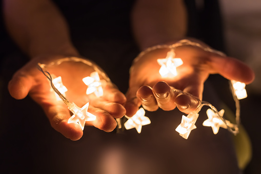 Hands holding shiny Christmas lights with star shapes