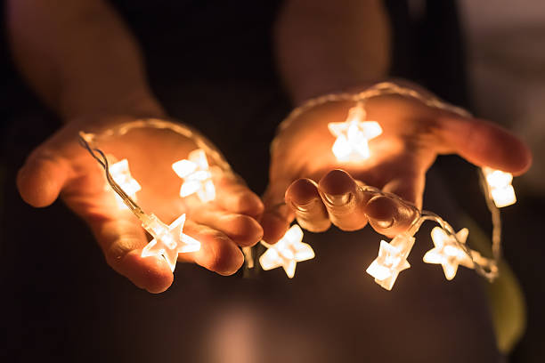 ręce trzymające błyszczące świąteczne światła z kształtami gwiazd - christmas christmas ornament human hand decoration zdjęcia i obrazy z banku zdjęć