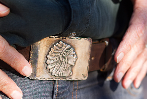 A close-up shot of a vintage Southwest silver belt buckle, blue jeans, and a man's hands.