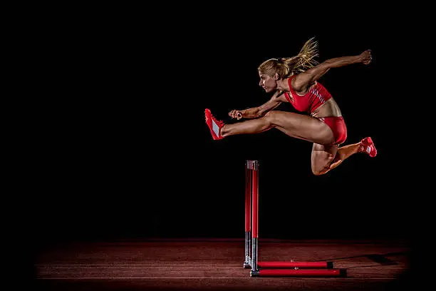 Female athlete jumping over hurdle.
