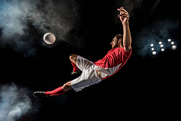 Soccer player kicking Soccer player kicking football in mid-air at night. soccer sport stock pictures, royalty-free photos & images