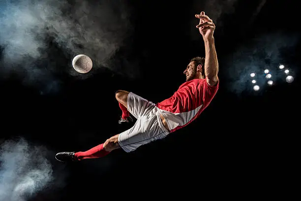 Soccer player kicking football in mid-air at night.