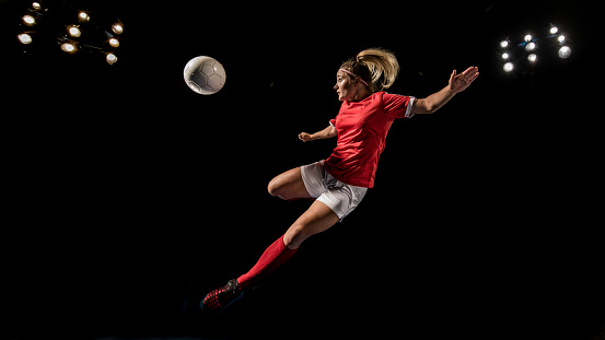 Soccer player kicking football in mid-air at night.