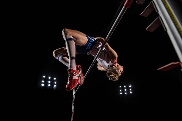 High jumper performing Young male high jumper clearing bar. horizontal bar stock pictures, royalty-free photos & images