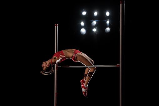 Young female high jumper clearing bar.