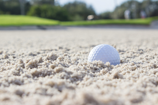 A golf ball in the sand trap of a beautiful golf course