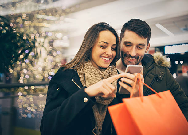 Happy couple shopping in the city with smartphone Happy couple shopping in the city with smartphone holiday shopping stock pictures, royalty-free photos & images