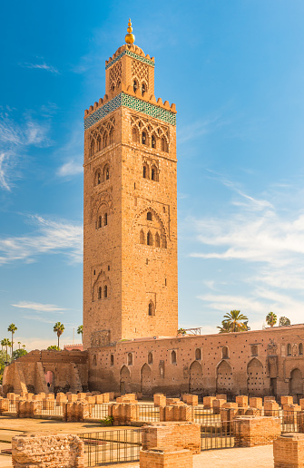 View of the  Koutoubia Mosque's (or Kutubiyya Mosque) minaret behind the orange and date palm trees of the Lalla Hasna Park. The largest mosque in Marrakesh, Morocco. Ornamented with curved windows, a band of ceramic inlay, pointed merlons, and decorative arches. Completed under the reign of the Berber Almohad Caliph Yaqub al-Mansur (1184 to 1199), and has inspired other buildings such as the Giralda of Seville and the Hassan Tower of Rabat.