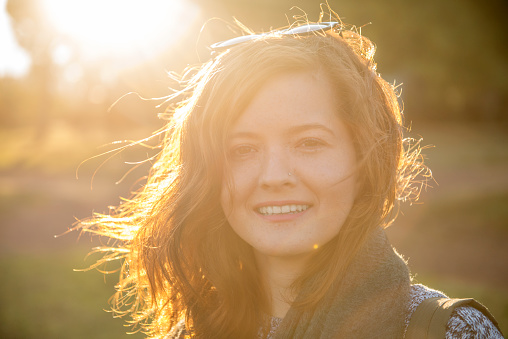 Portrait of laughing young woman under sunlight.  Horizontal composition. Smiling teenage girl in tree area looking at camera with positive facial expression. Image taken with Nikon D800 and developed from RAW format.