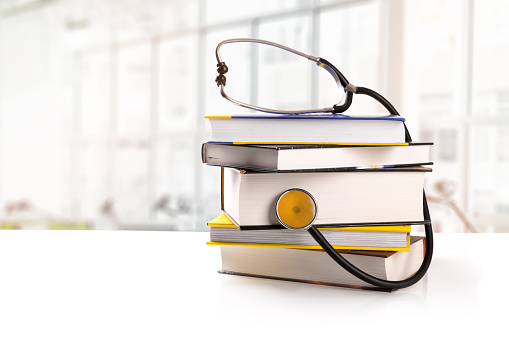 medical education - stack of books with stethoscope on the table in library