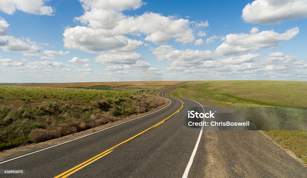 Long Winding Road Cury into The Distance Vanishing Point A central Washington State road winds out into the distance below fluffy blue clouds Road Stock Photo