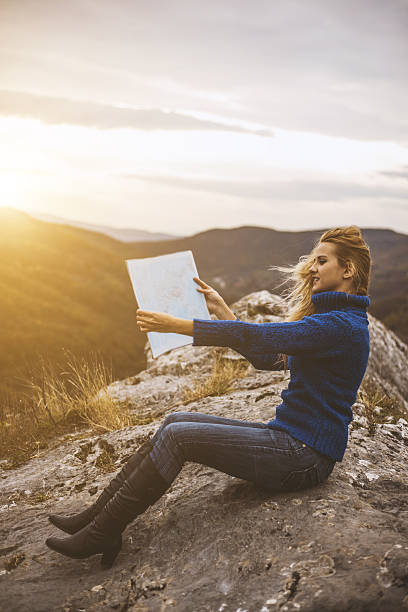 istock Young woman with map sitting on the rock at sunset. 636907390