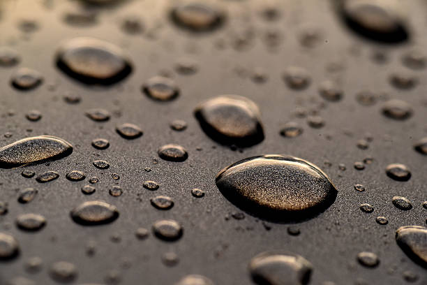 rain drops on a blue car hood.Water drops on the hood of a automobile with clouds reflected of of the windshield.