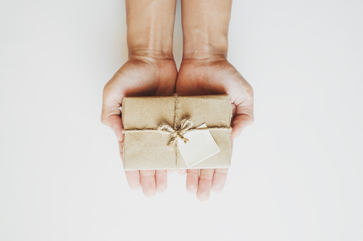 Hand holding parcel post gift box, with blank paper note, on white table background