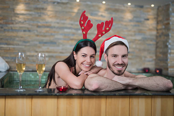 jovem casal usando chapéus de natal na banheira olhando para a câmera - couple hot tub spa treatment health spa - fotografias e filmes do acervo