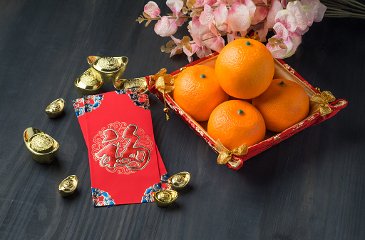 Chinese New year,red envelope packet (ang pow) with gold ingots and oranges and flower on brown wood table top,Chinese Language mean Happiness.