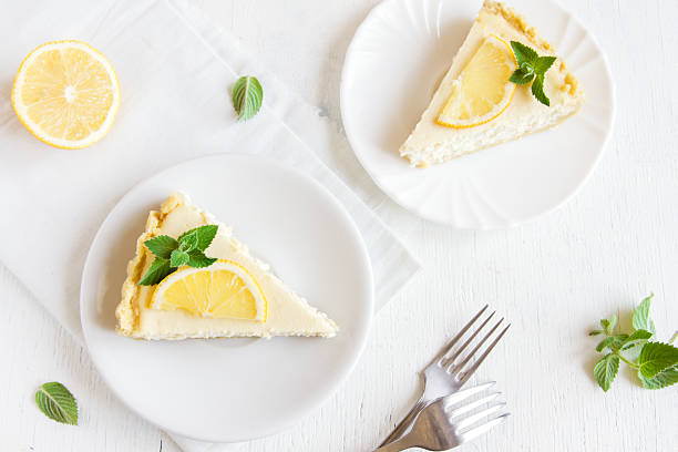 lemon cheesecake Pieces of delicious homemade lemon cheesecake with slices of lemon and mint on white background with copy space dessert sweet food stock pictures, royalty-free photos & images