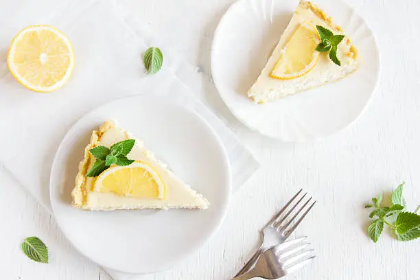 Pieces of delicious homemade lemon cheesecake with slices of lemon and mint on white background with copy space