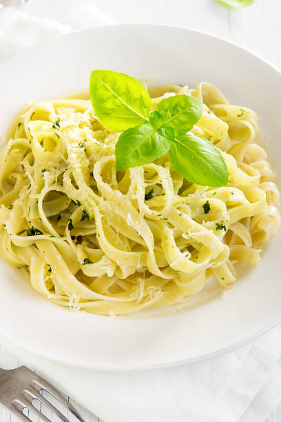 Tagliatelle pasta with pesto sauce, cheese and basil leaves on white plate close up - healthy homemade pasta