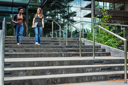 Two young female college students walking down steps of a university campus together.