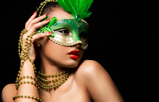 Upscale Indian woman wearing gold jewellery and red lipstick on black background. Green party mask.