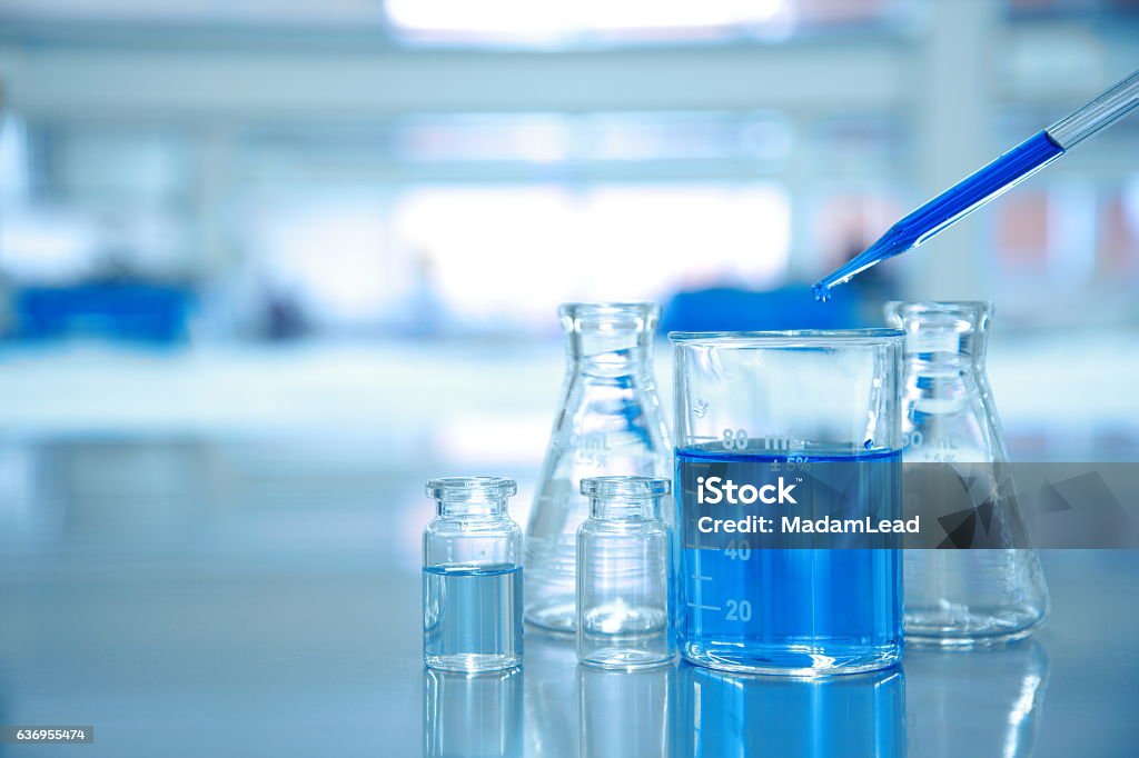 blue drop into glass beaker with flask and science laboratory blue drop into glass beaker with flask and science laboratory background Laboratory Stock Photo