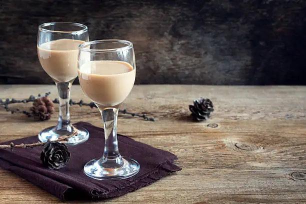 Irish cream coffee liqueur, Christmas decoration and cones over rustic wooden background - homemade festive Christmas alcoholic drink