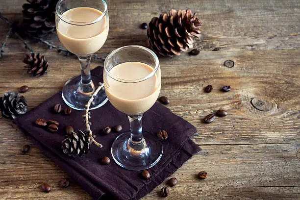 Irish cream coffee liqueur with coffee beans, Christmas decoration and cones over rustic wooden background - homemade festive Christmas alcoholic drink