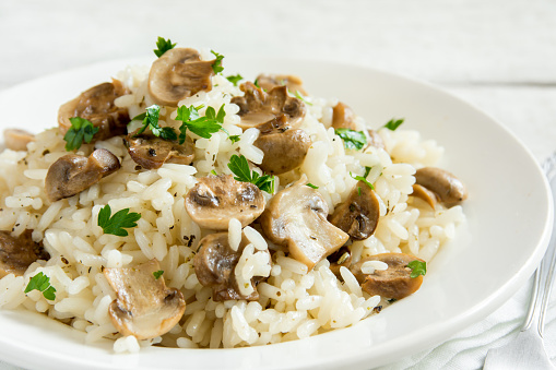 Mushroom risotto with parsley on white wooden background - healthy vegetarian food
