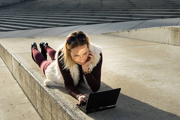 mulher deitada do lado de fora em degraus, segurando laptop na natureza da cidade - staircase steps moving down student - fotografias e filmes do acervo