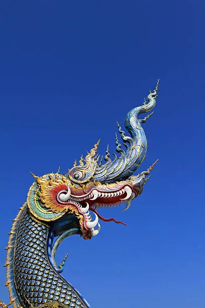 The blue head of Naka or serpent statue opening mouth with blue sky background at Wat Rong Sua Ten at Chiang Rai, Thailand - Buddhist Temple 