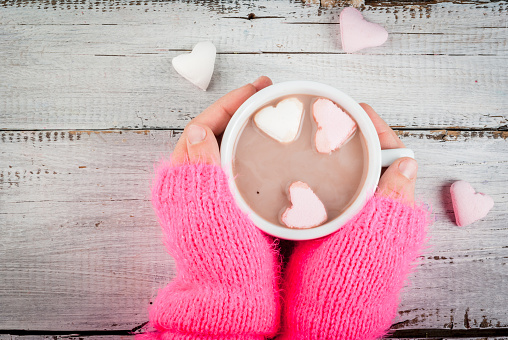 Girl drinking hot chocolate with marshmallows in the shape of hearts, Valentine's Day celebration, hands in the picture, top view, copy space