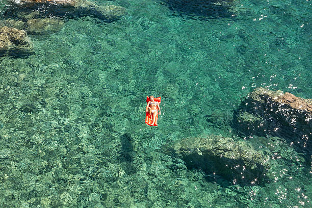 Young woman relaxing on floating mattress above sea Aerial view of a young woman floating on pool mattress in the ocean. pool raft stock pictures, royalty-free photos & images