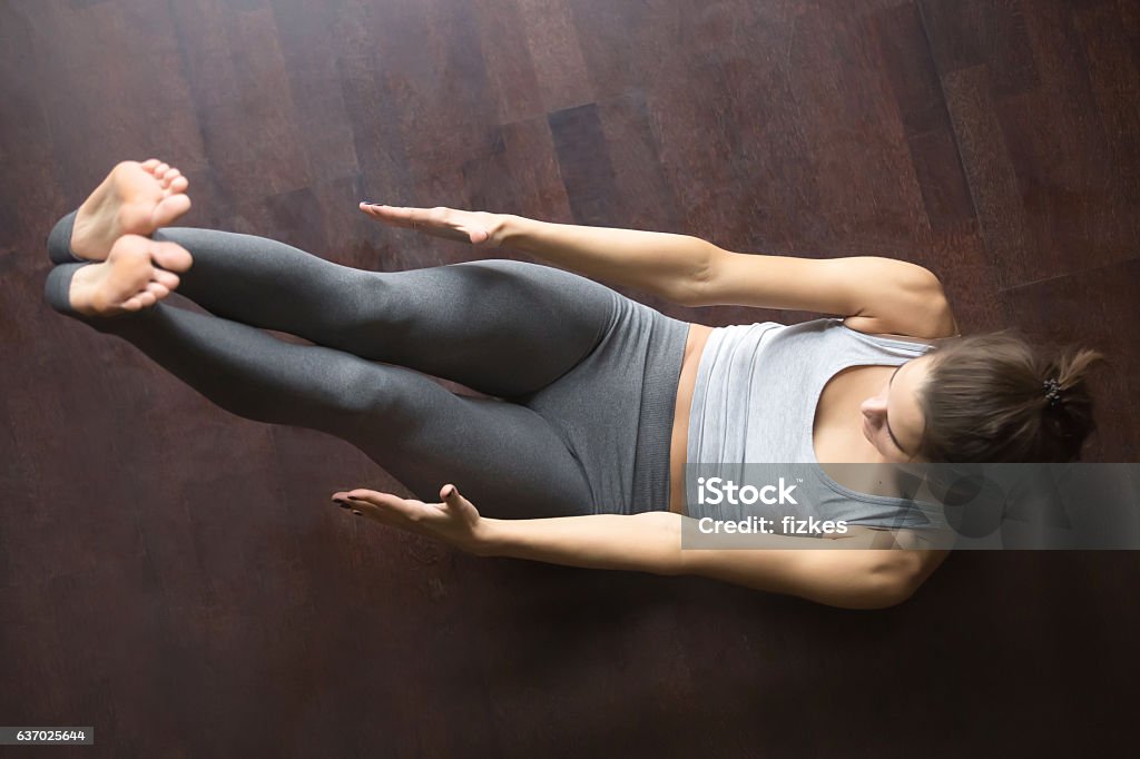 View from above. Abdominal crunches Beautiful young model working out at home, doing fitness exercise on floor, Paripurna Navasana for upper and lower abs, Full Boat pose. Core training. Top view. Full length Boat Position Stock Photo